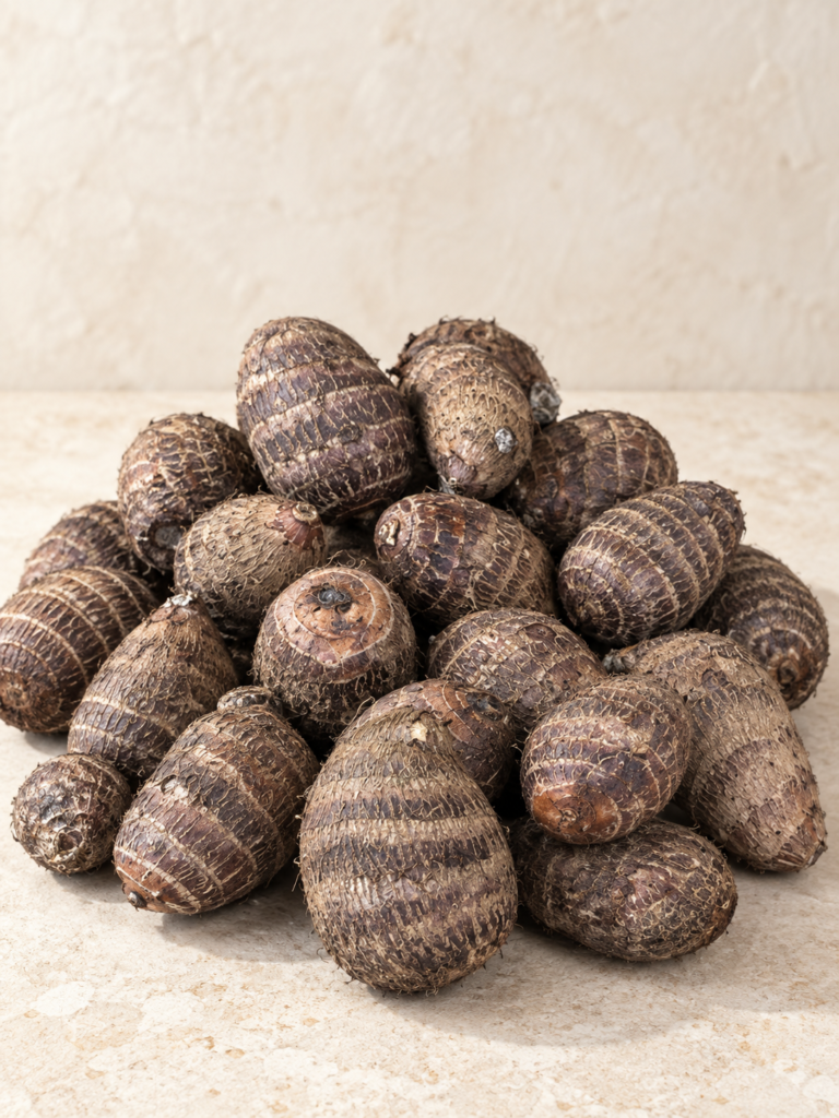Whole Ede cocoyam tubers arranged on a neutral stone surface